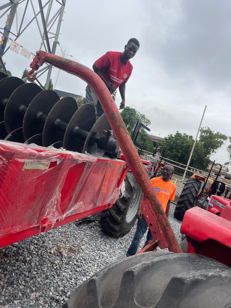 Worker attaching a disc harrow to a tractor hitch before delivery