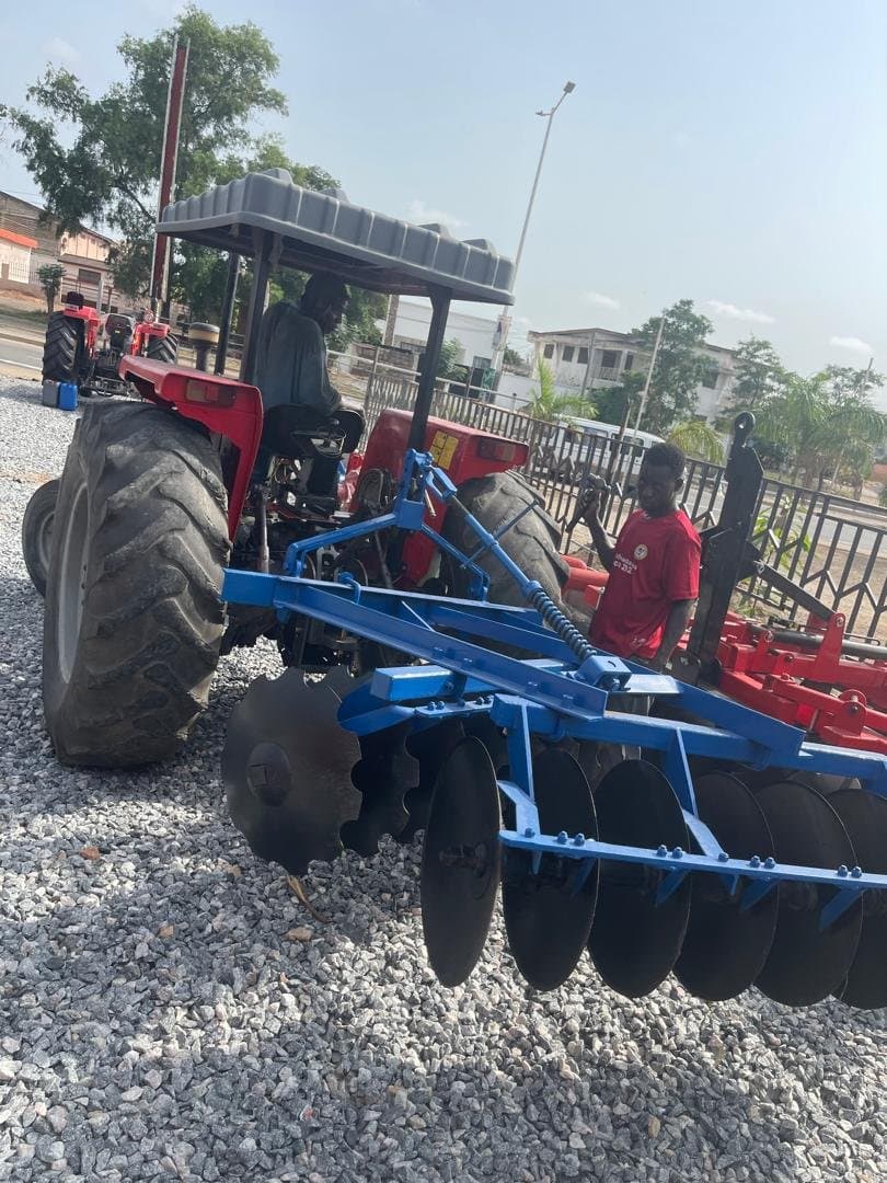 Tractor fitted with a blue disc harrow in the yard